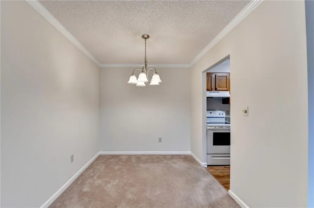 Unfurnished dining area featuring a textured ceiling, crown molding, carpet flooring, and a notable chandelier