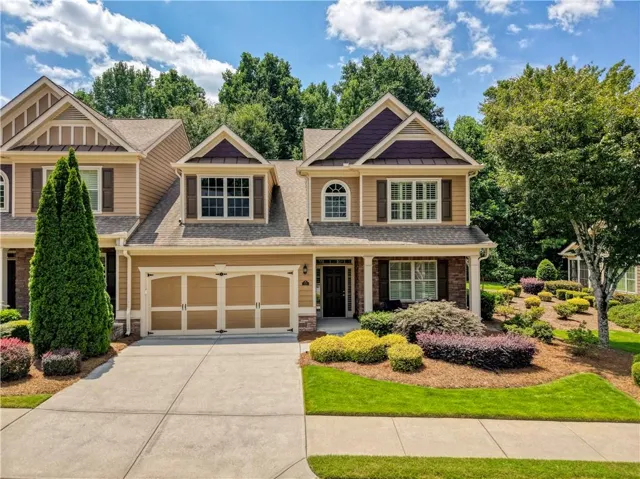 Two-story residence featuring a two-car garage with carriage-style doors, stone accents, and a covered front entry