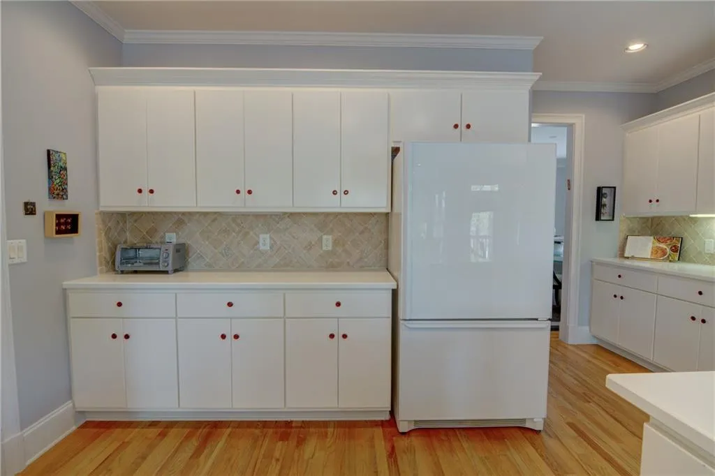 Kitchen with freestanding refrigerator, ornamental molding, white cabinetry, light wood-style flooring, and decorative backsplash