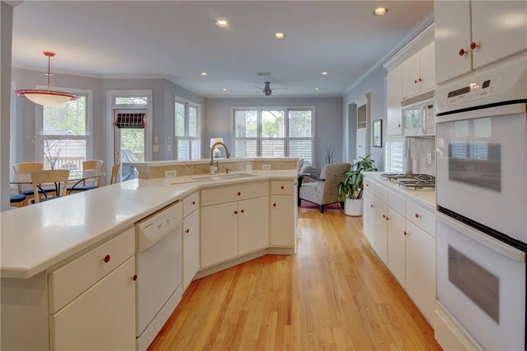 Kitchen featuring white appliances, white cabinets, light wood finished floors, a center island with sink, and hanging light fixtures