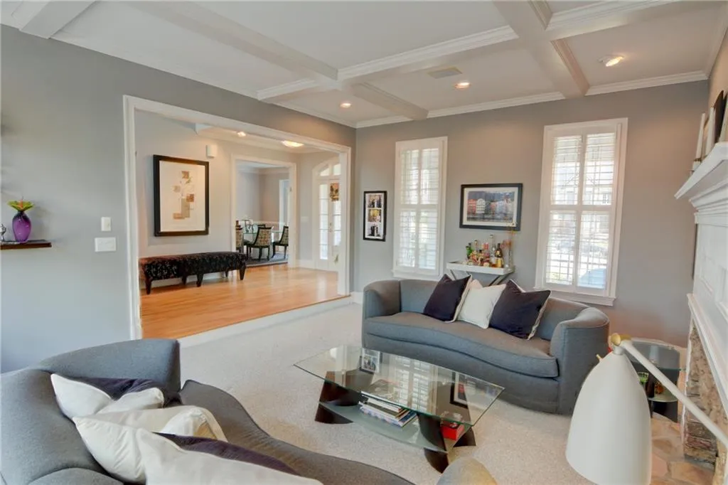 Living room with a fireplace, coffered ceiling, recessed lighting, crown molding, and light colored carpet