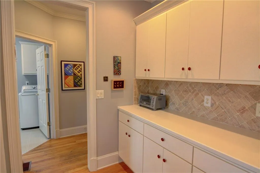 Kitchen with light countertops, washer / dryer, light wood-type flooring, white cabinets, and tasteful backsplash