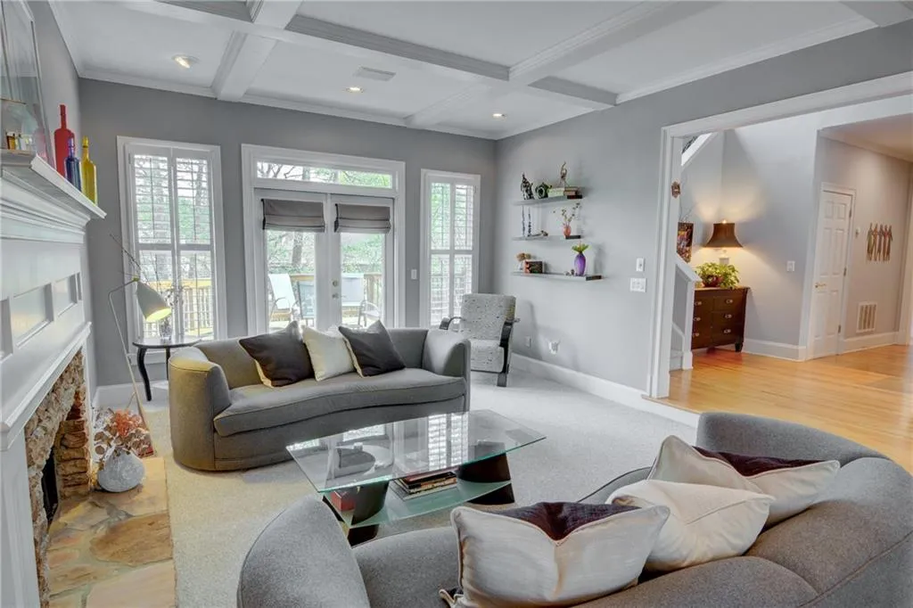 Living area featuring a fireplace with raised hearth, coffered ceiling, ornamental molding, recessed lighting, and french doors