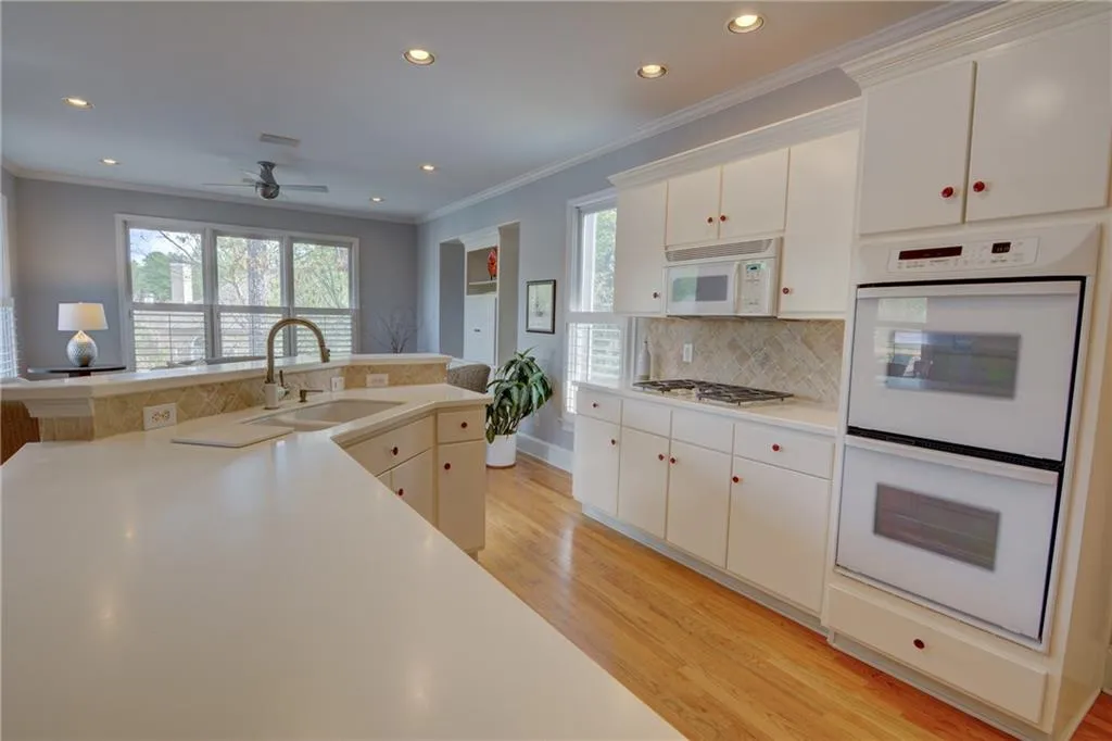 Kitchen with white appliances, light countertops, light wood-style flooring, ornamental molding, and recessed lighting
