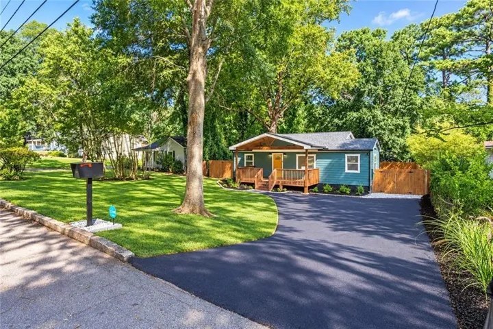 Exterior featuring a wooden front porch, teal siding, gray shingle roof, and a paved driveway