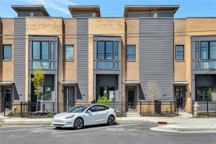 Modern townhome exterior featuring a brick facade, horizontal panel siding, black framed windows, and a flat roofline