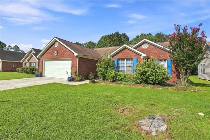 Brick exterior with contrasting blue shutters, attached garage, and mature landscaping
