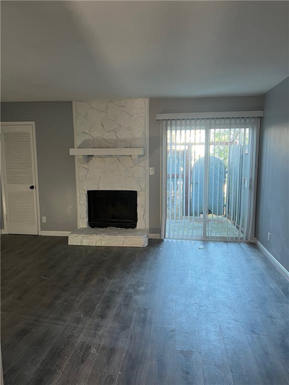 Unfurnished living room with dark hardwood / wood-style floors and a stone fireplace