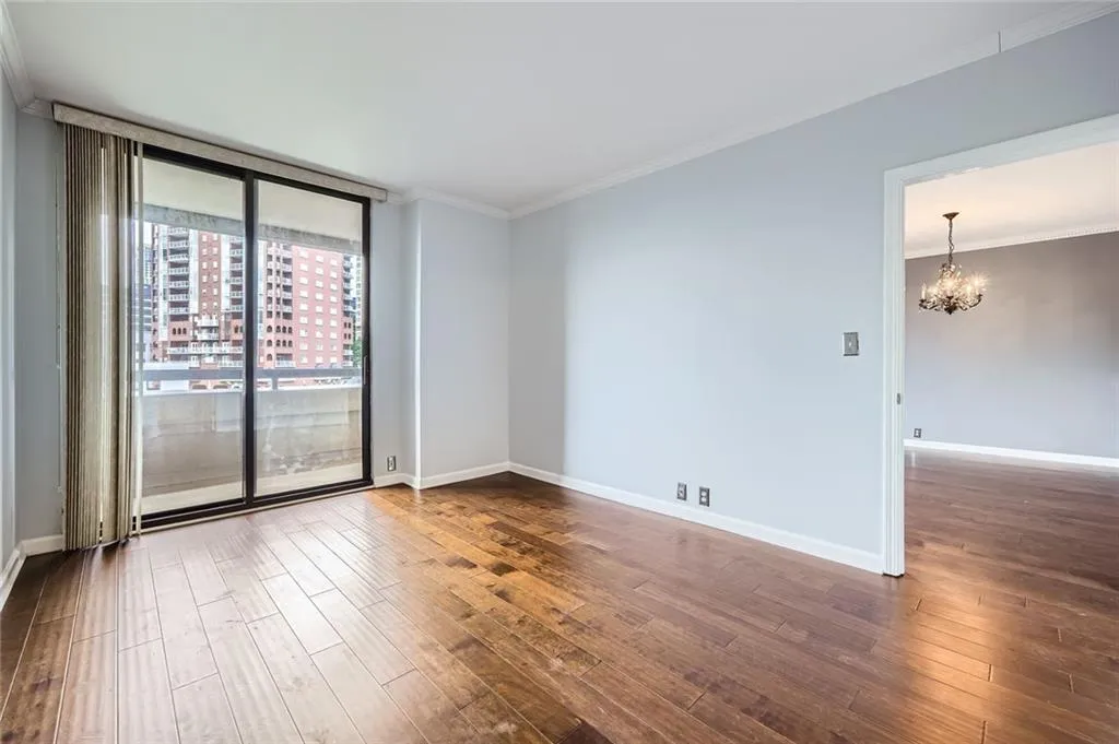 Empty room with a chandelier, dark wood-style flooring, ornamental molding, baseboards, and a wall of windows