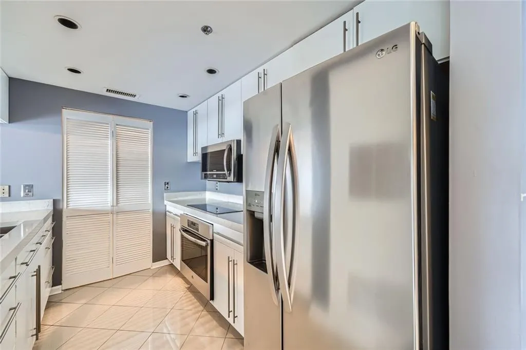 Kitchen featuring stainless steel appliances, light countertops, white cabinetry, light tile patterned floors, and baseboards