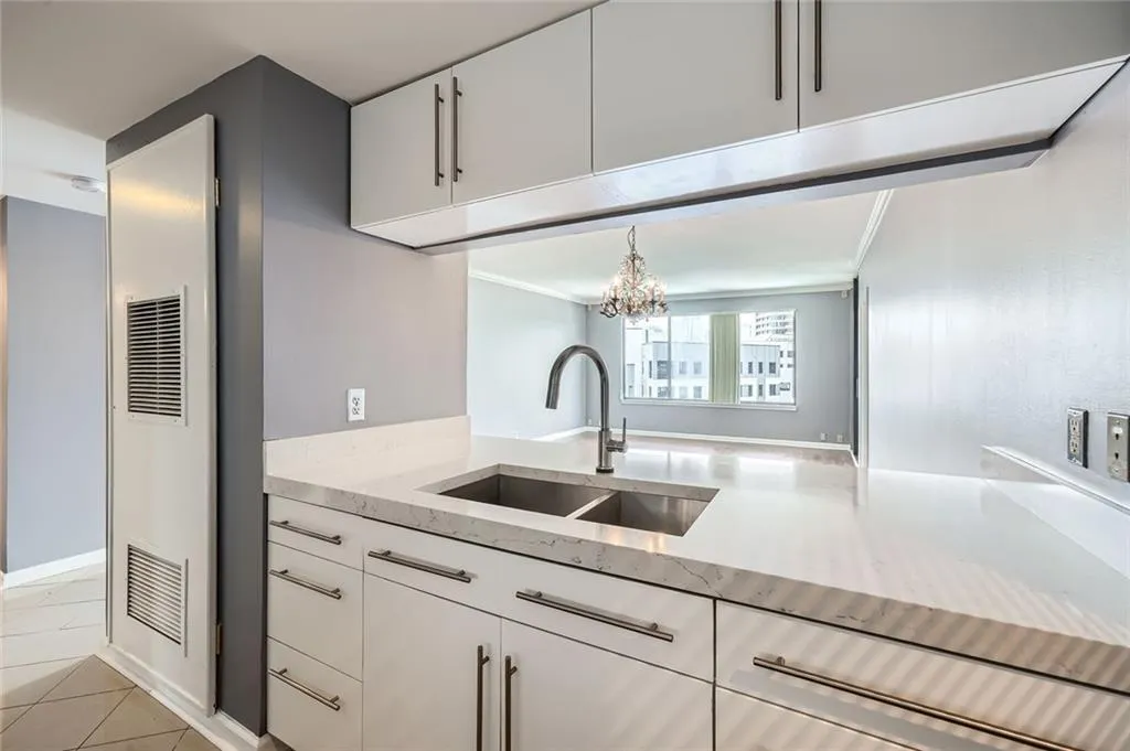 Kitchen featuring a sink, a heating unit, light stone counters, white cabinets, and a chandelier
