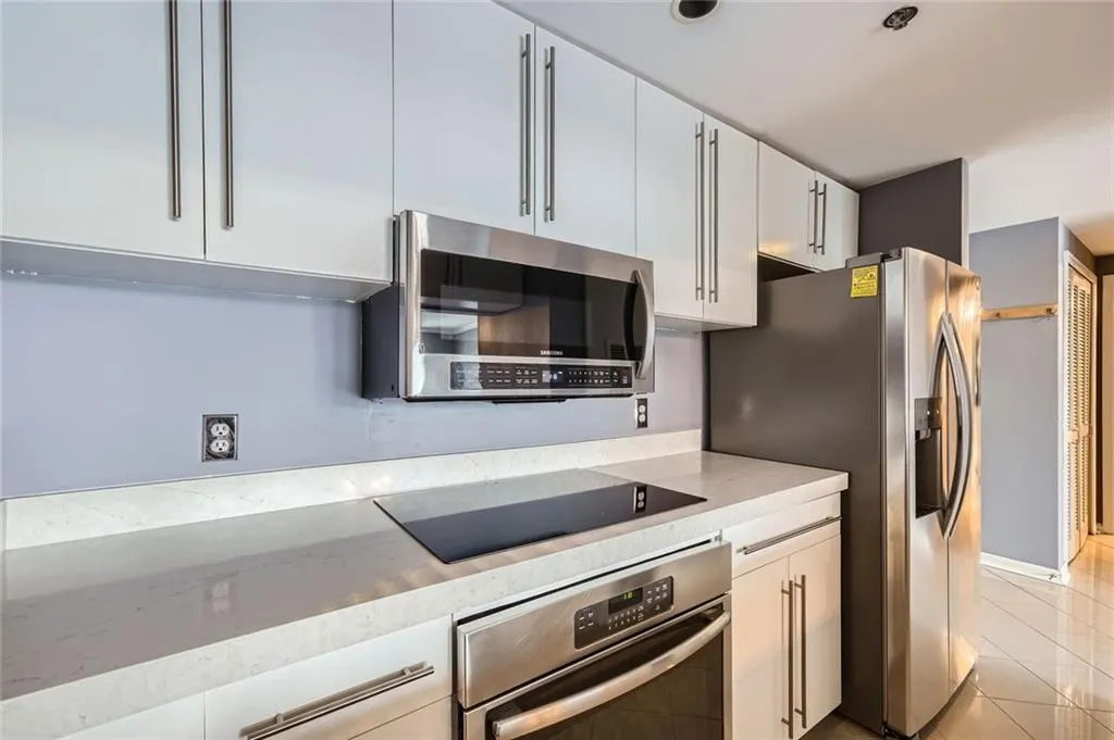 Kitchen with appliances with stainless steel finishes, light tile patterned floors, white cabinets, and light stone counters
