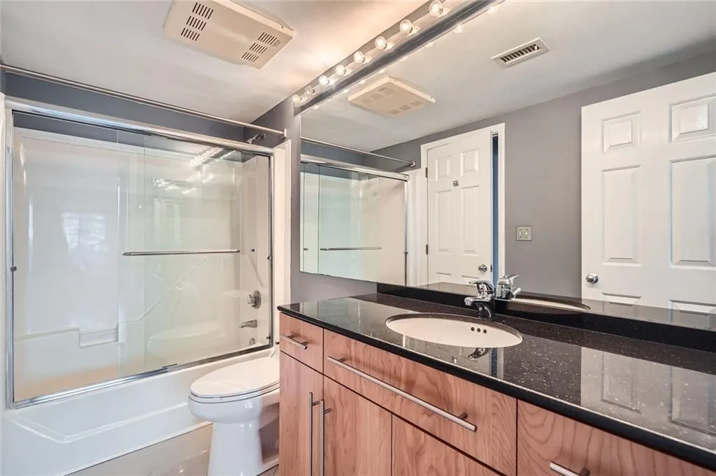 Bathroom with vanity, toilet, and bath / shower combo with glass door