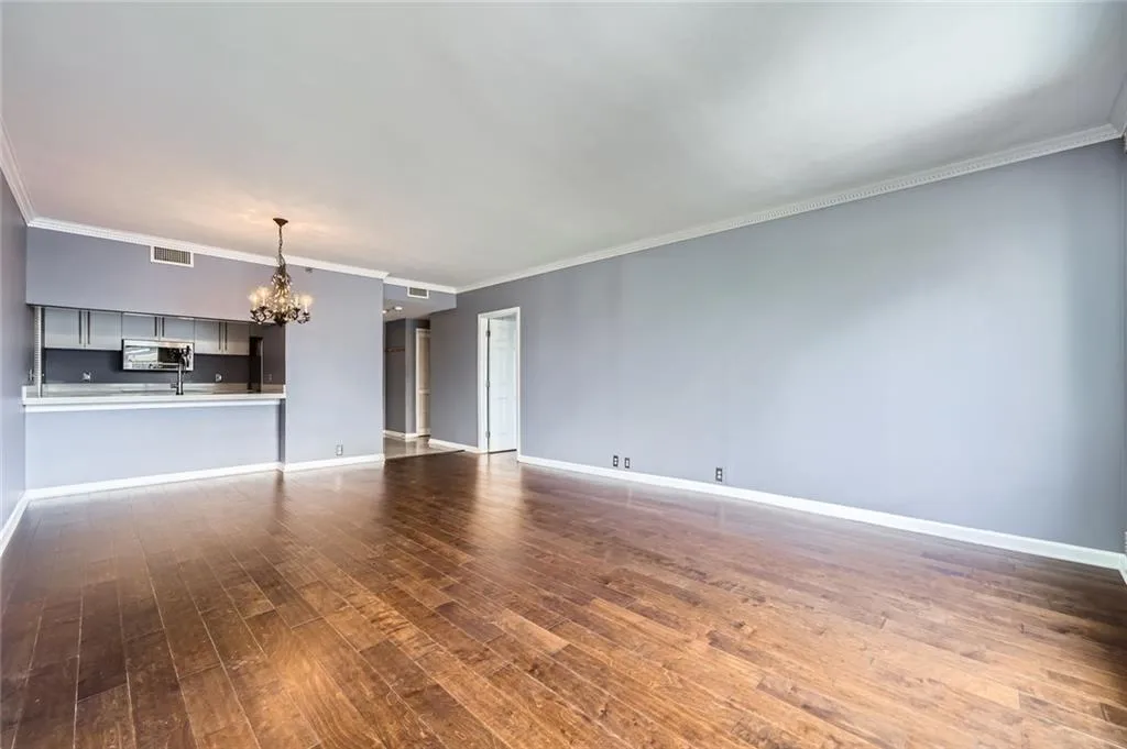 Unfurnished living room with a chandelier, dark wood-style flooring, baseboards, and crown molding