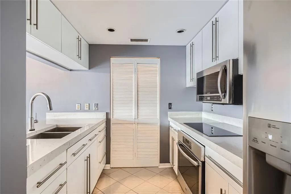Kitchen featuring stainless steel appliances, a sink, light tile patterned floors, white cabinetry, and light stone countertops