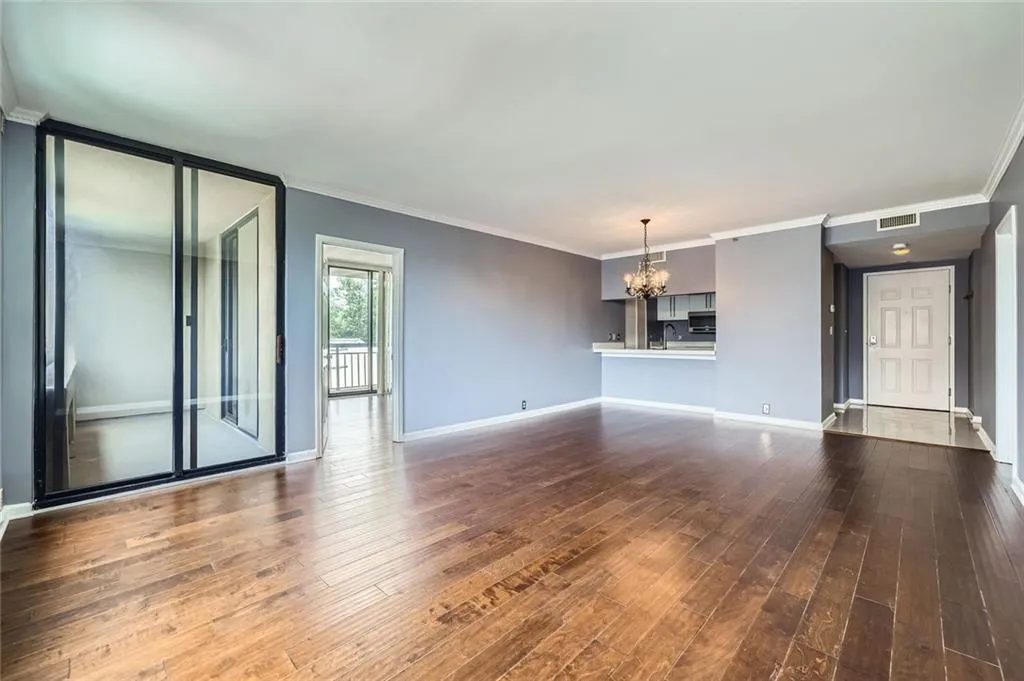 Unfurnished living room with a chandelier, dark wood-style floors, baseboards, and crown molding