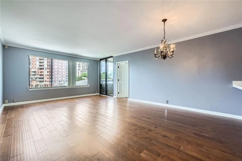 Empty room featuring a chandelier, ornamental molding, dark wood-type flooring, and baseboards