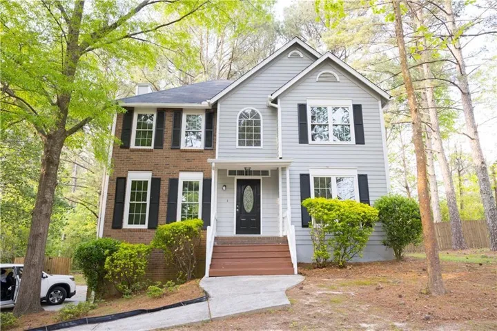 Two-story exterior featuring brick and siding accents, multiple windows with dark shutters, and a prominent front entrance with wooden steps