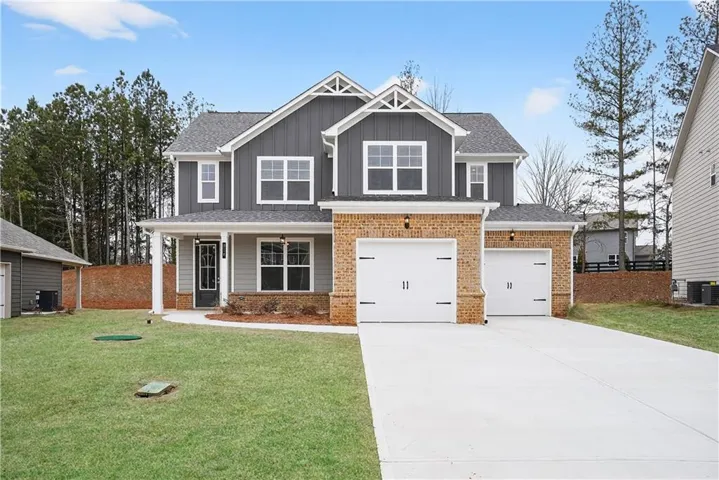 Two-story residence featuring a gray and brick exterior, a covered front porch with white columns, and a two-car garage with white doors
