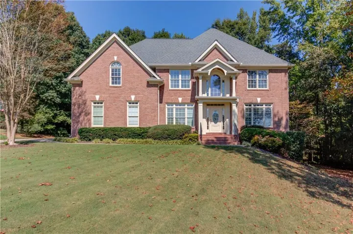 Brick exterior with an arched window, a covered entrance, a second-story balcony, and a sloped, landscaped lawn