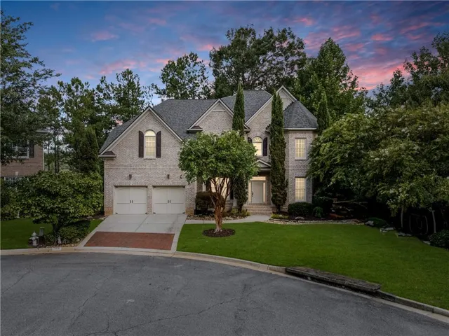 Brick exterior residence featuring a two-car garage, manicured lawn, and mature trees