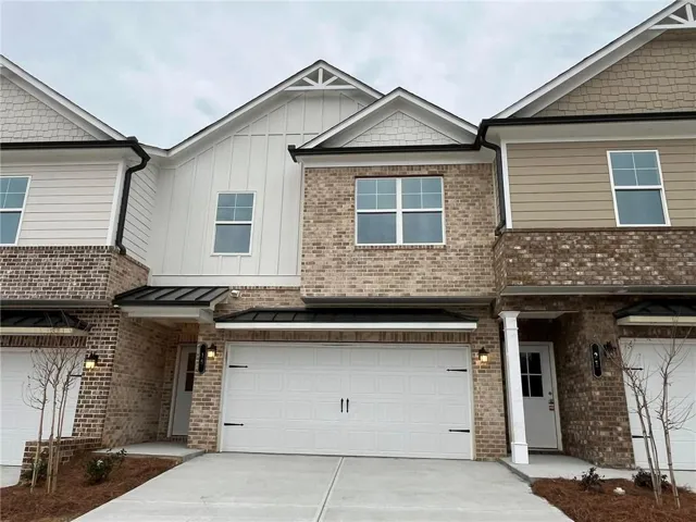 Townhome / multi-family property featuring driveway, a standing seam roof, board and batten siding, an attached garage, and brick siding