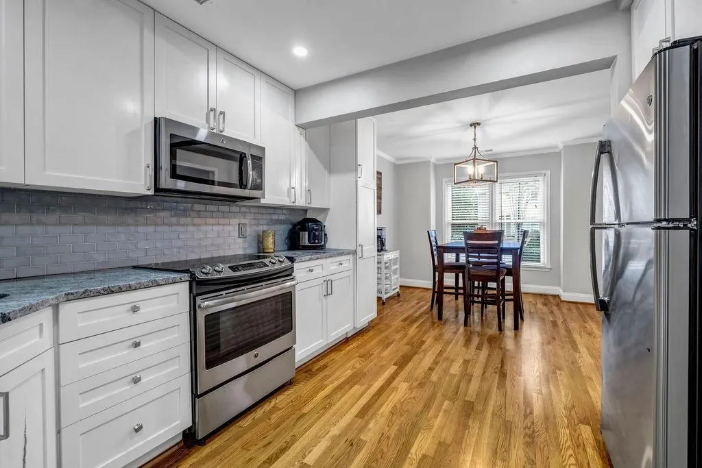 Kitchen with crown molding, decorative backsplash, stainless steel appliances, light wood-style floors, and white cabinetry