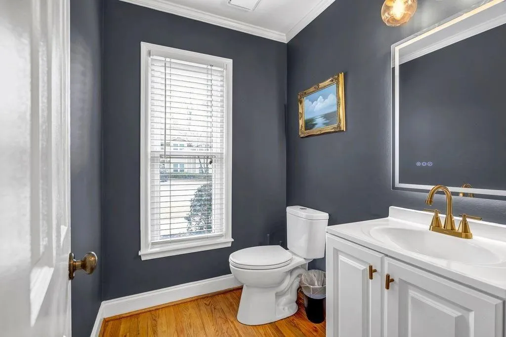 Half bathroom with toilet, ornamental molding, wood finished floors, baseboards, and vanity