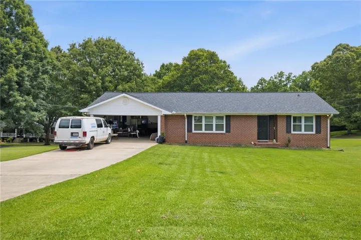 Brick exterior with a dark shingle roof, white trim, and a covered carport