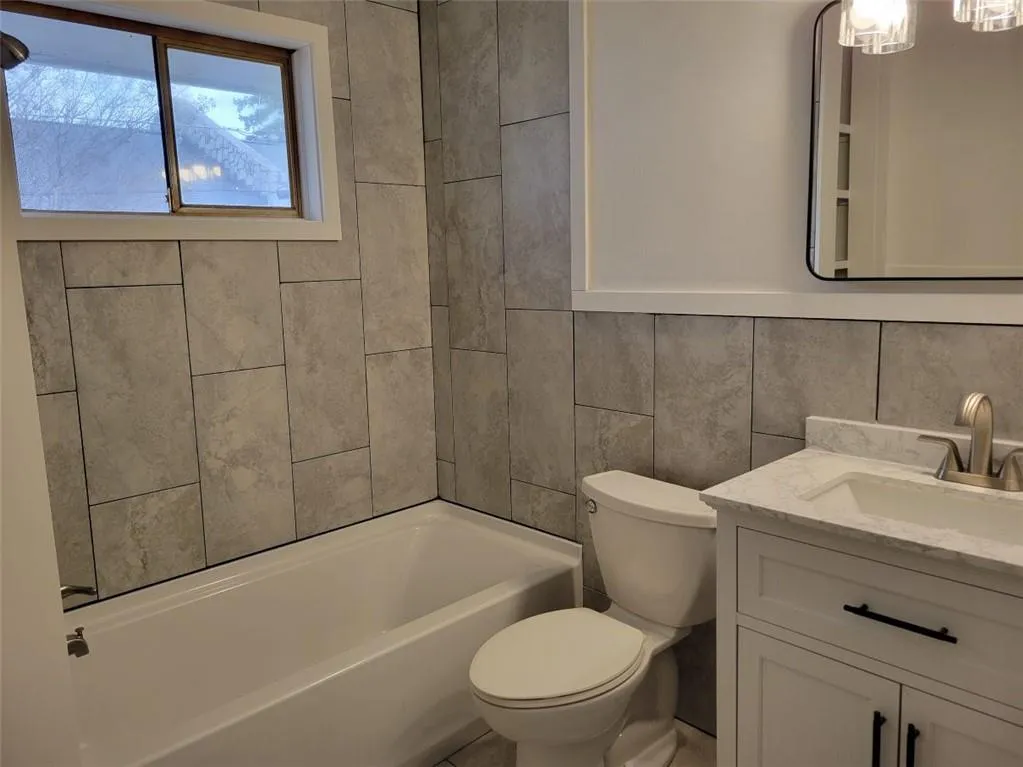 Bathroom featuring bathtub / shower combination, toilet, vanity, and tile walls
