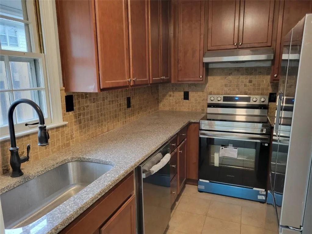 Kitchen featuring a sink, backsplash, under cabinet range hood, and appliances with stainless steel finishes