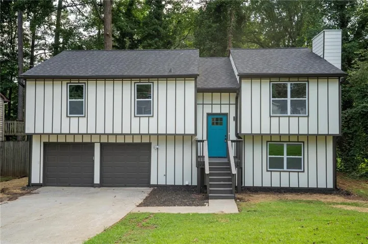 Two-story exterior featuring white vertical siding with dark trim, a vibrant blue entry door, and a two-car garage with dark doors