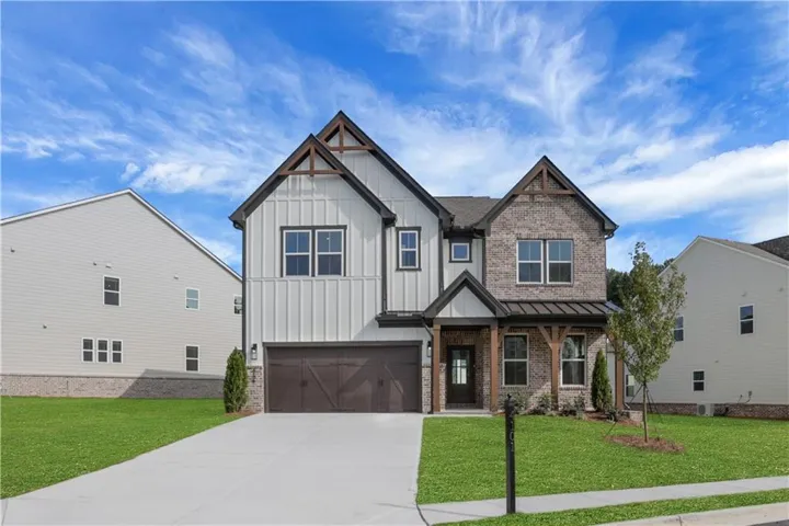 Multi-material facade featuring vertical siding and brick, covered entry with wood-tone columns, attached garage with wood-tone door, and a concrete driveway