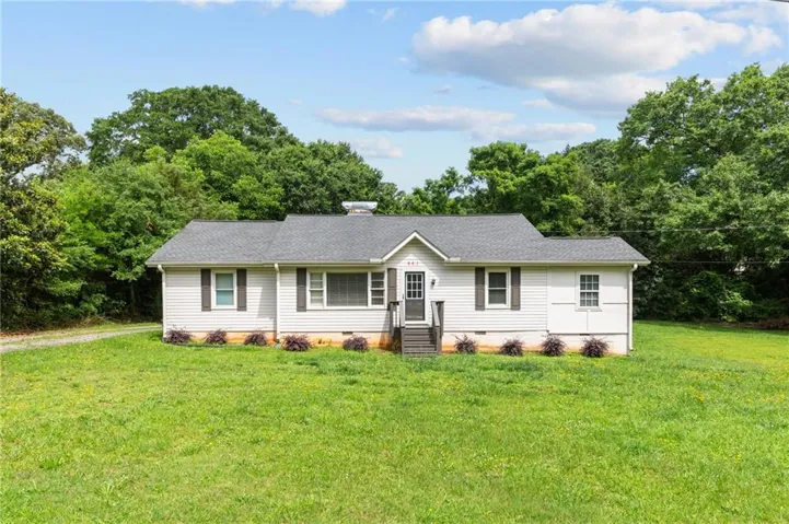 White siding exterior, dark gray shingle roof, dark brown shutters, front entry porch, and a gravel driveway