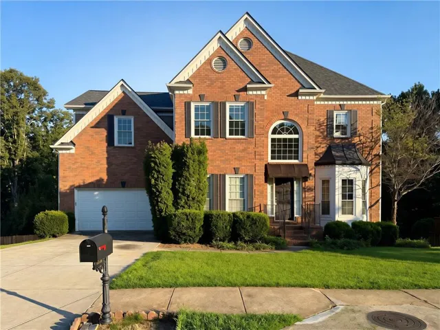 Brick exterior with decorative shutters, arched window, front entry awning, bay window, and attached garage