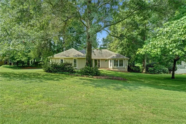 Expansive green lawn with mature trees and a single-story residence featuring light-colored siding, a gabled roof, and multiple windows