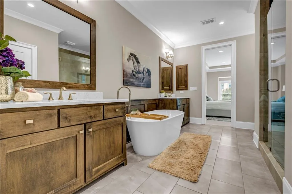 Bathroom featuring two vanities, light tile patterned floors, a freestanding tub, crown molding, and recessed lighting