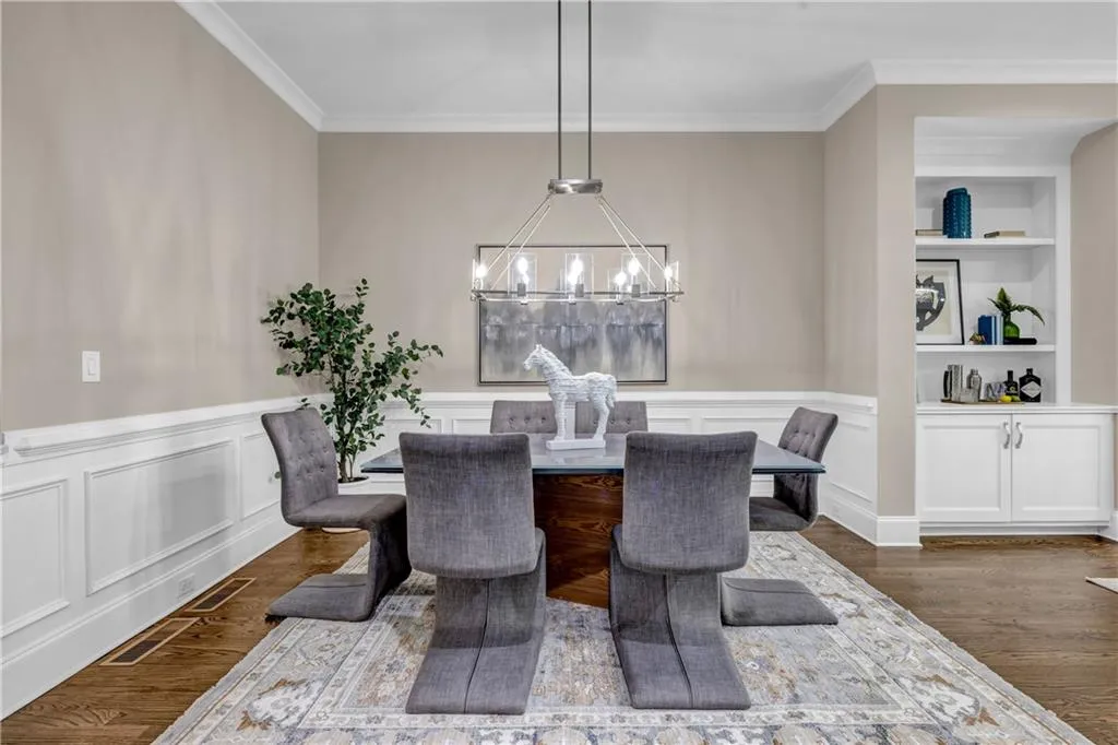 Dining area featuring dark wood-type flooring, ornamental molding, built in shelves, a wainscoted wall, and a decorative wall