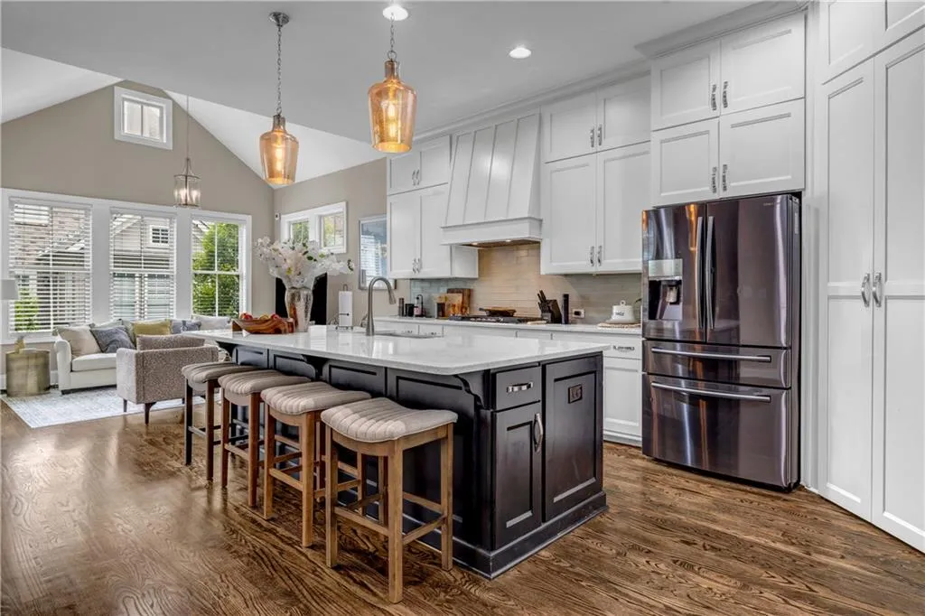 Kitchen featuring stainless steel fridge with ice dispenser, white cabinetry, a breakfast bar, decorative light fixtures, and dark wood finished floors
