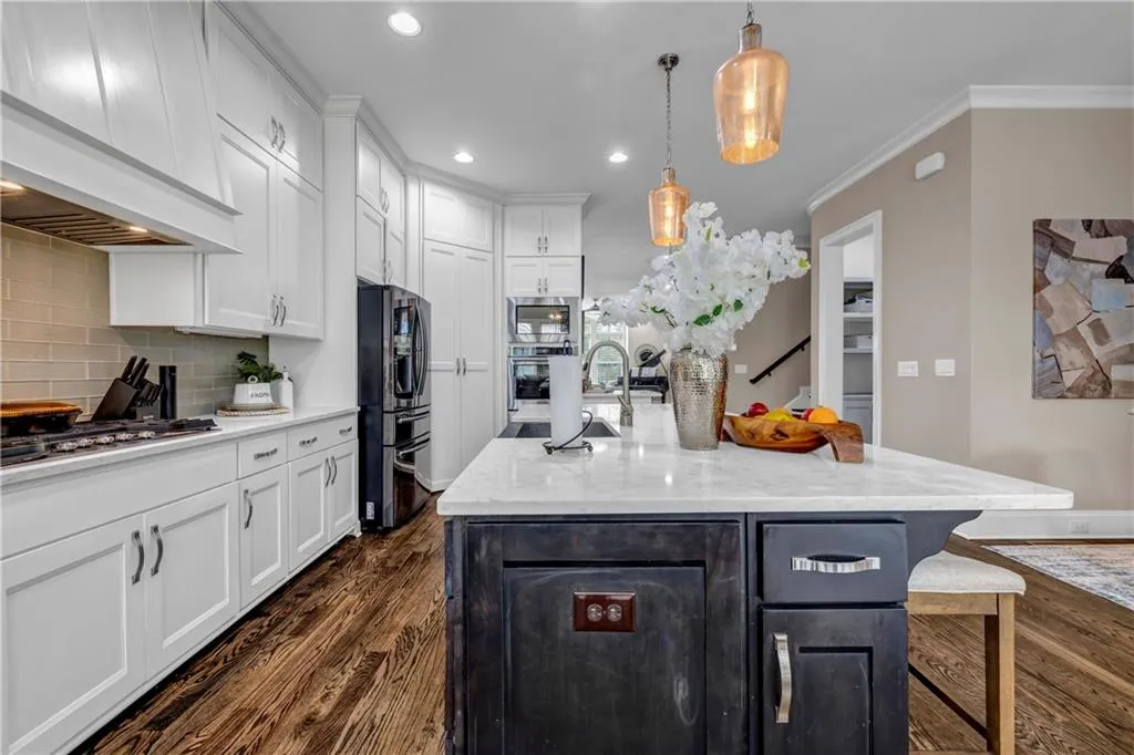 Kitchen featuring white cabinetry, dark wood-style flooring, light stone counters, ornamental molding, and a center island with sink