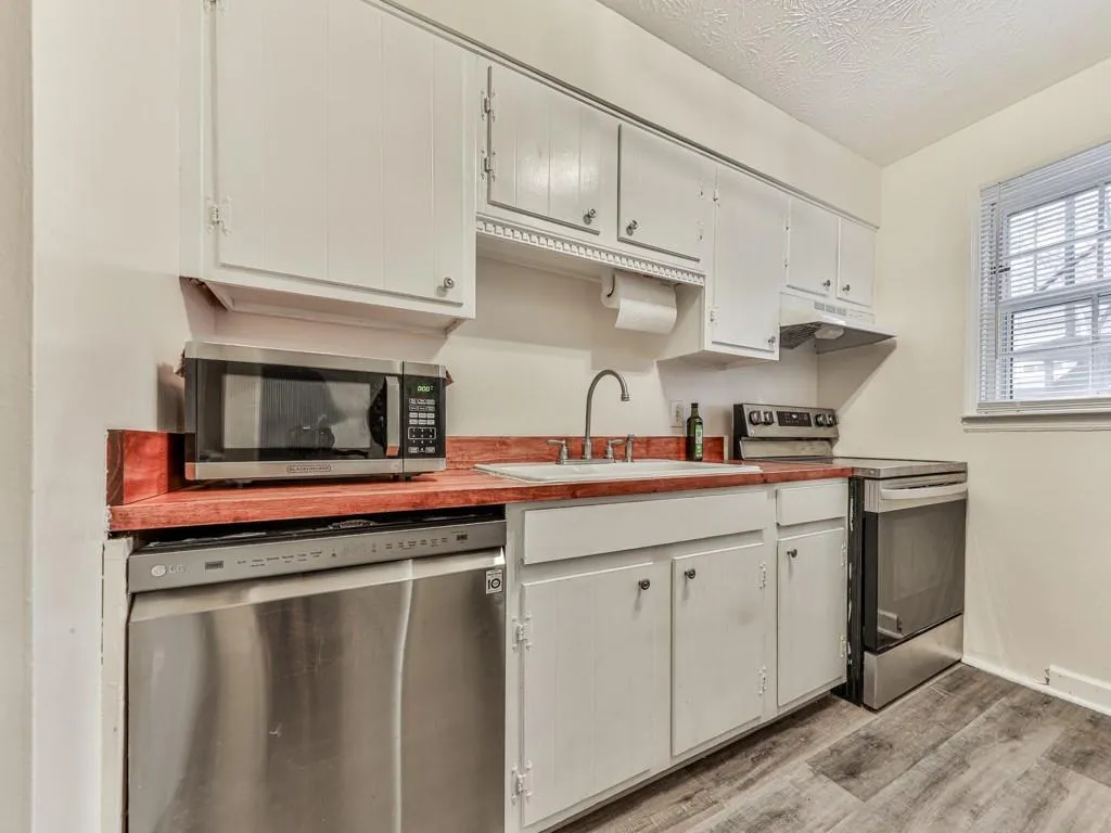 Kitchen featuring stainless steel appliances, light wood-type flooring, a textured ceiling, under cabinet range hood, and white cabinets