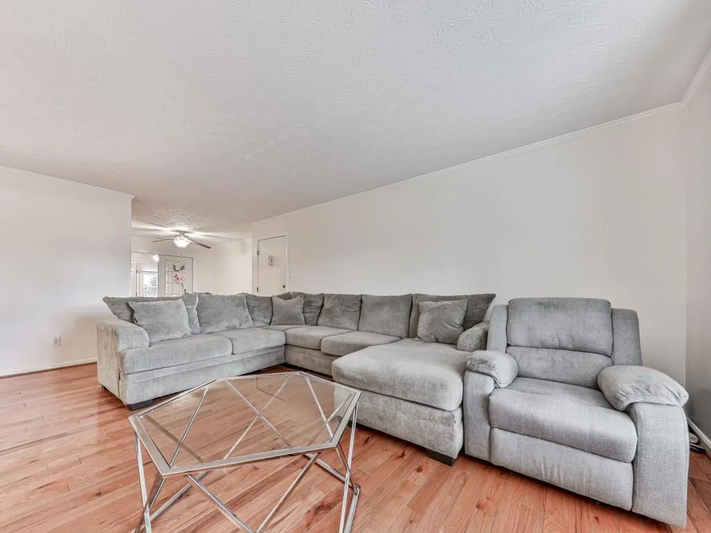 Living area featuring light wood-style floors, a textured ceiling, a ceiling fan, and ornamental molding