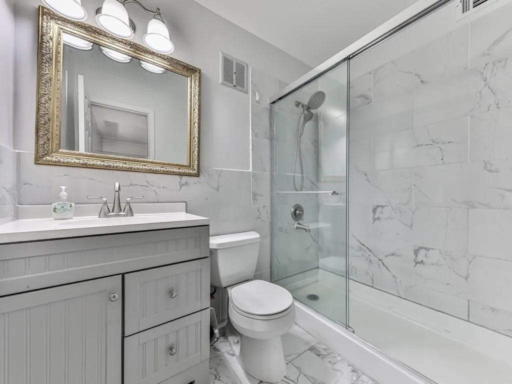 Full bath with tile walls, a marble finish shower, vanity, and light marble finish flooring