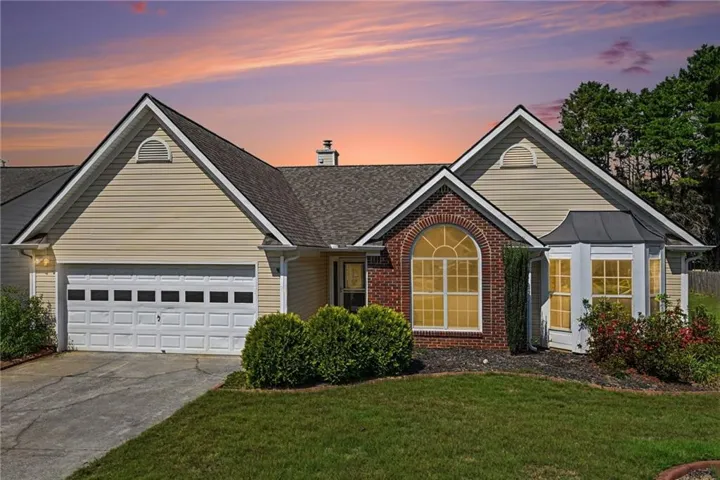 Single-story residence featuring a two-car garage, brick facade accents, a prominent arched window, and a bay window with a metal roof