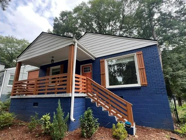 Brick exterior with a vibrant blue finish, covered front porch, wooden railings, and decorative window shutters