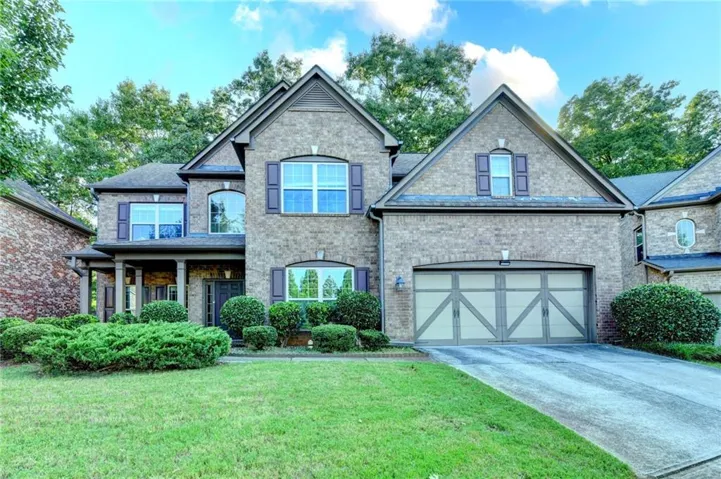 Brick facade with arched windows, a covered entry porch, a two-car garage, and established landscaping