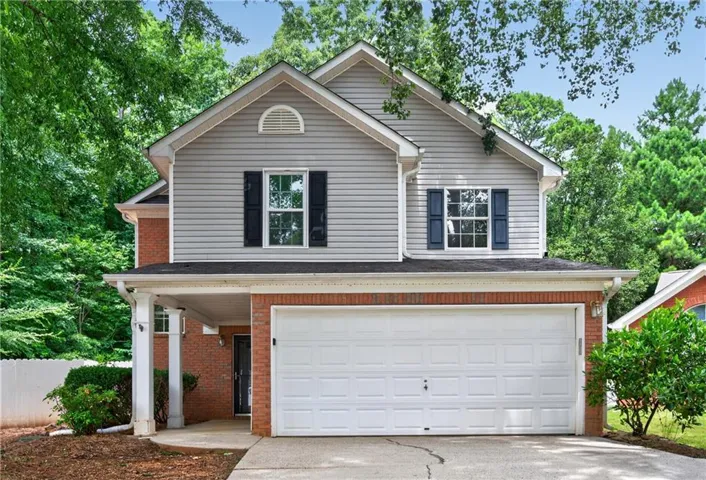 Two-story residence featuring a two-car garage, brick and siding exterior, front entry porch with columns, and dark window shutters