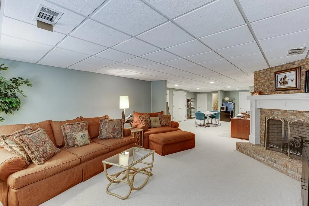 Living room featuring a drop ceiling, a brick fireplace, and carpet floors