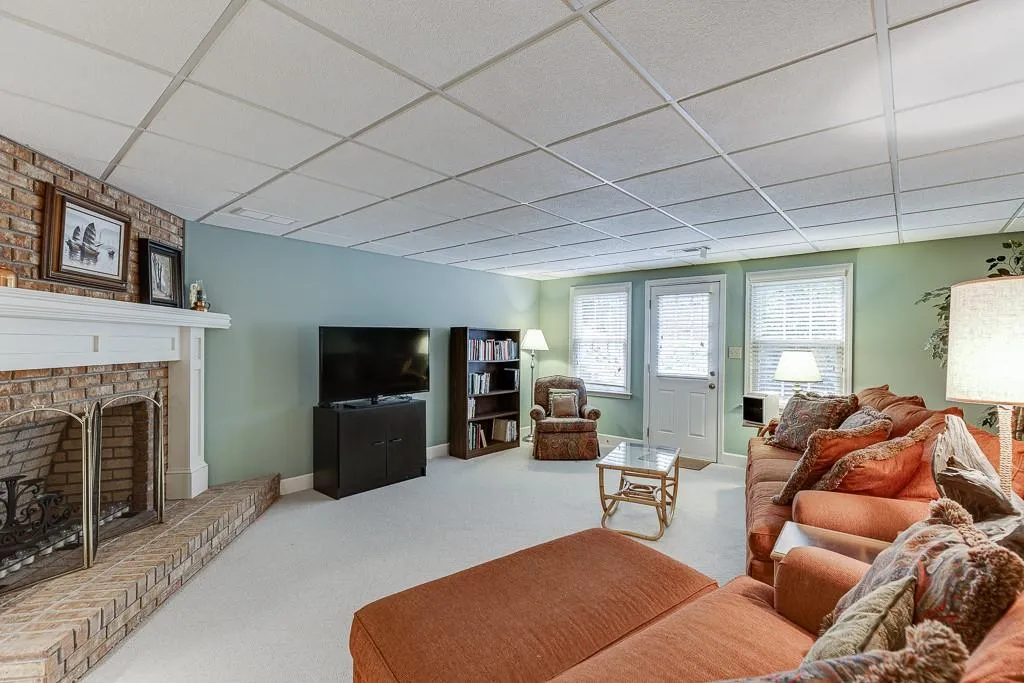 Living room featuring a brick fireplace, a paneled ceiling, and carpet flooring