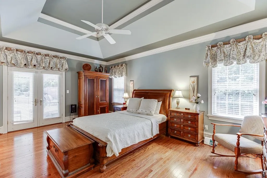Bedroom with ceiling fan, a raised ceiling, light hardwood / wood-style floors, ornamental molding, and access to exterior